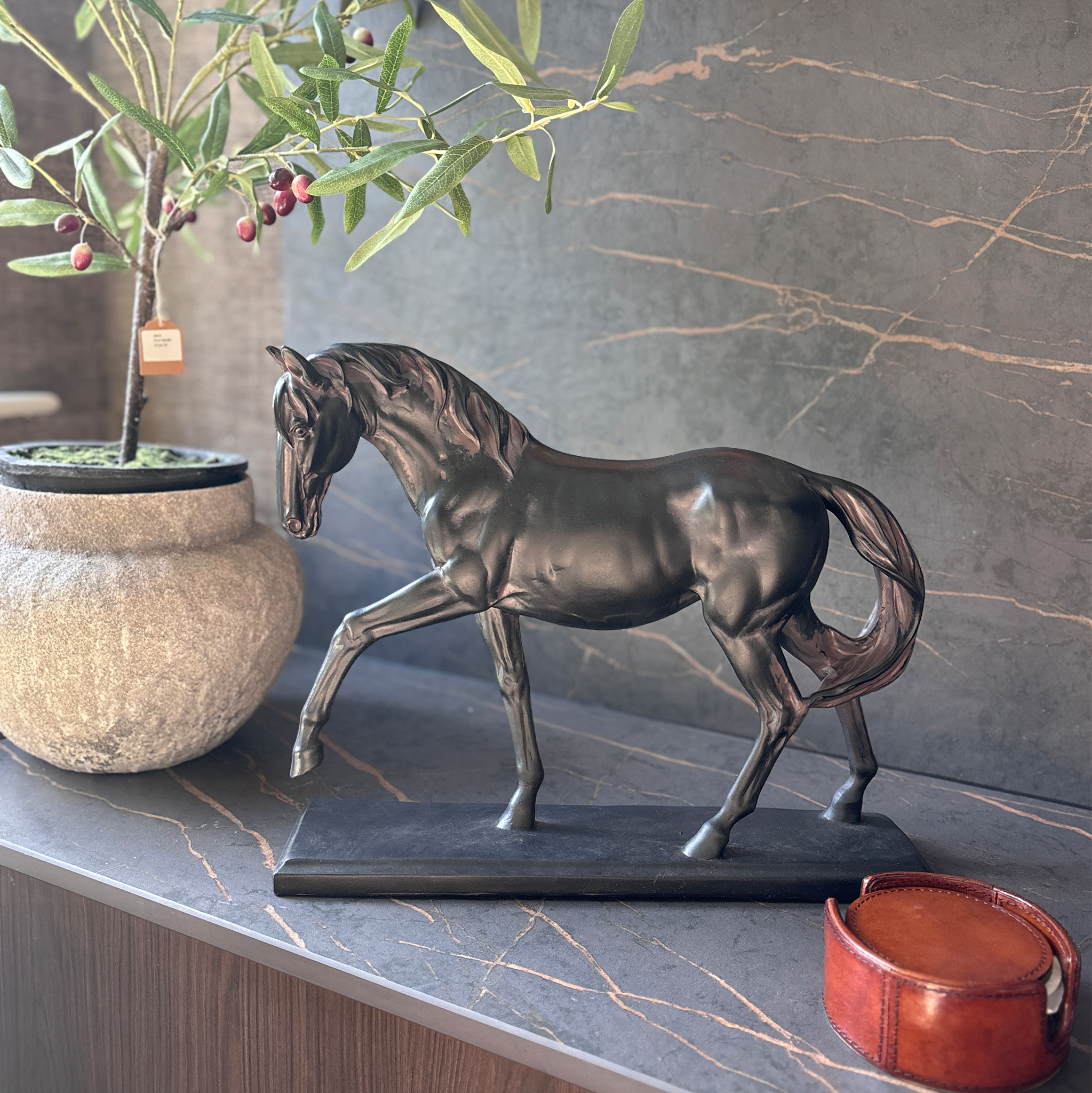 A black horse figurine, in a proud, mid-stride pose. Mounted on a matching rectangular plinth, with a deliberately distressed finish