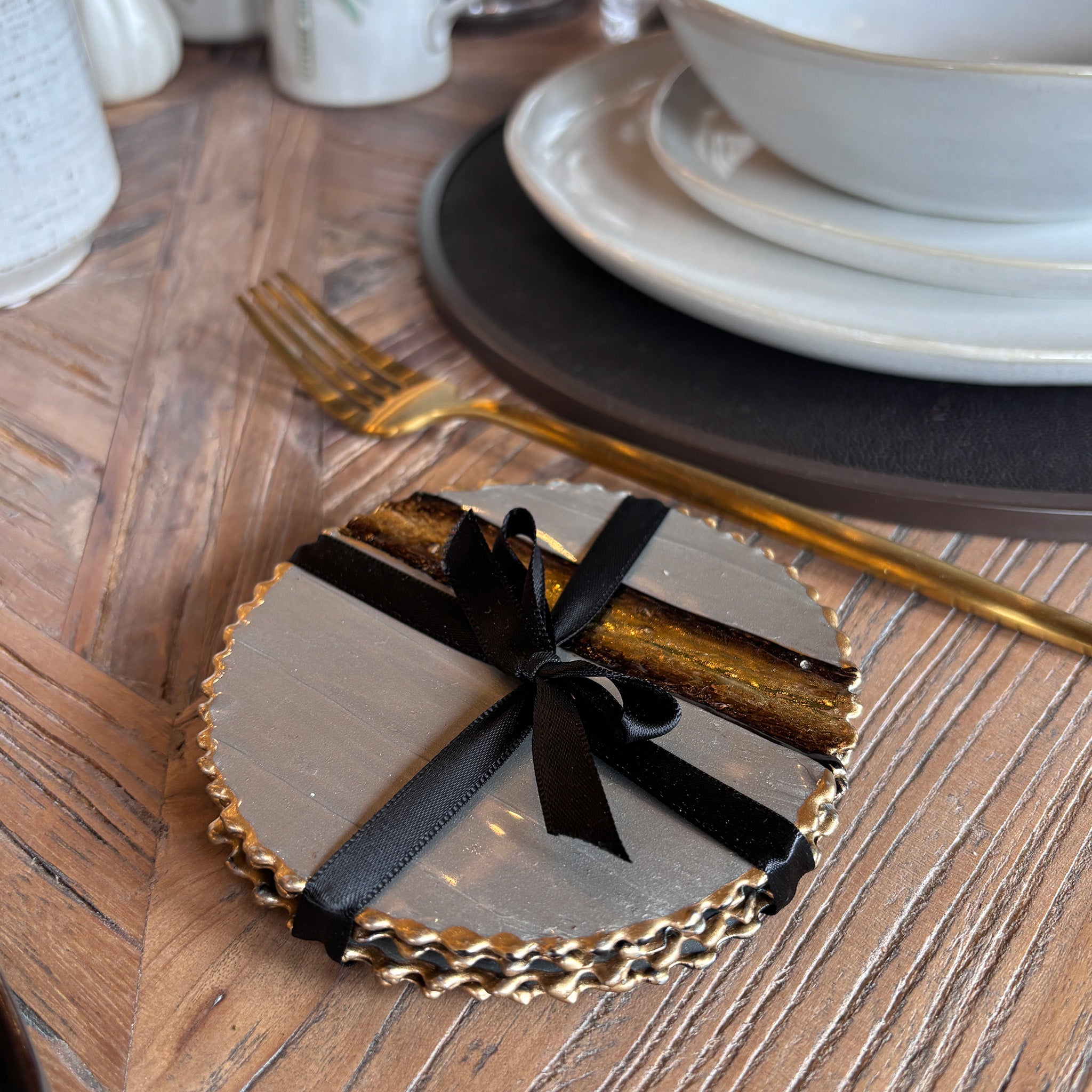 A luxurious set of round enamel-coated coasters featuring a smooth light grey surface with a striking gold-edged rim. 
