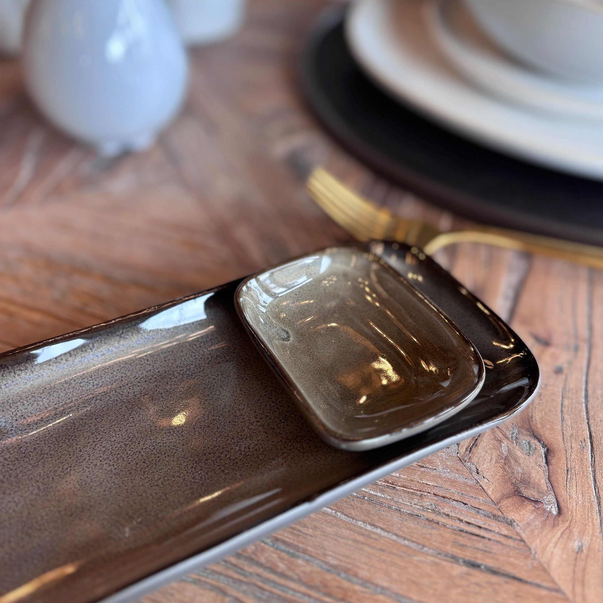 A rectangular serving tray with an integrated dip bowl, finished in a reactive glaze that creates a natural, mottled bronze and brown effect. Each piece will vary slightly in colour and pattern, making every one unique.